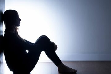 Une femme est assise adossée à un mur dans un environnement sombre