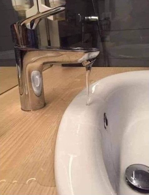 A washbasin with water leaking from the tap next to it.